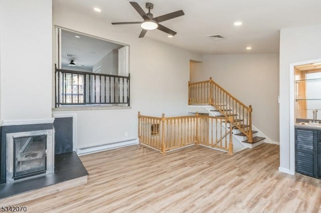 interior space with a baseboard heating unit, wood finished floors, visible vents, and a ceiling fan