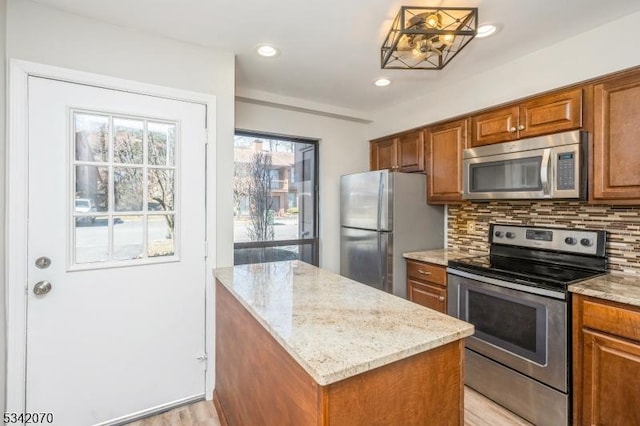 kitchen featuring light stone counters, decorative backsplash, brown cabinets, and appliances with stainless steel finishes