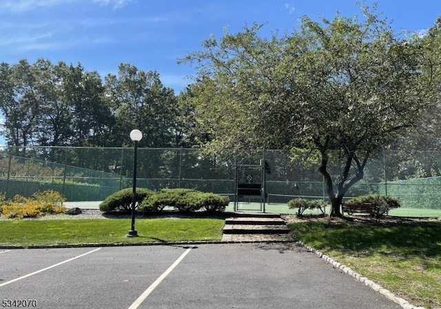 view of tennis court featuring a gate, a yard, and fence