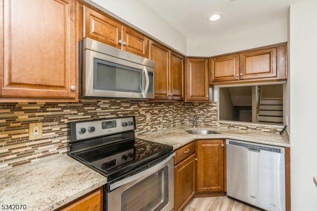 kitchen with brown cabinetry, backsplash, appliances with stainless steel finishes, and a sink