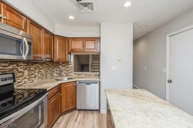 kitchen featuring visible vents, light wood-style flooring, a sink, backsplash, and stainless steel appliances