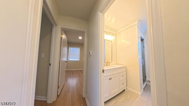 hallway with light wood-type flooring, baseboards, and a sink