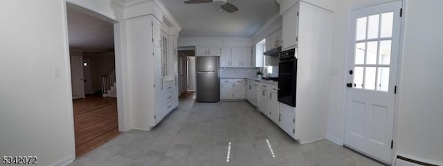 kitchen featuring tasteful backsplash, under cabinet range hood, freestanding refrigerator, white cabinetry, and a baseboard radiator