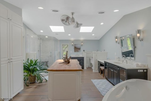 full bath featuring a freestanding bath, vaulted ceiling with skylight, wood finished floors, and a stall shower