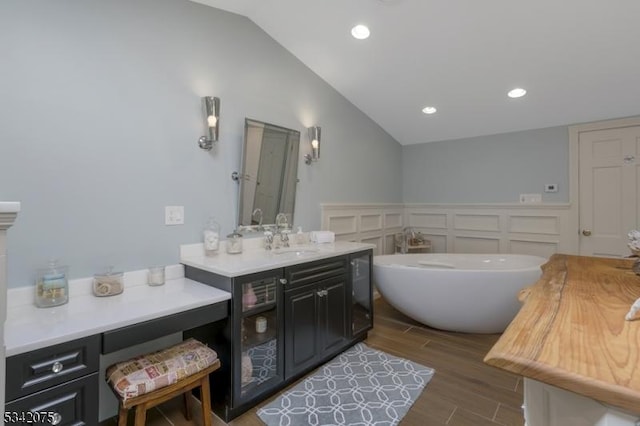 bathroom featuring wood finished floors, vaulted ceiling, a freestanding tub, and recessed lighting