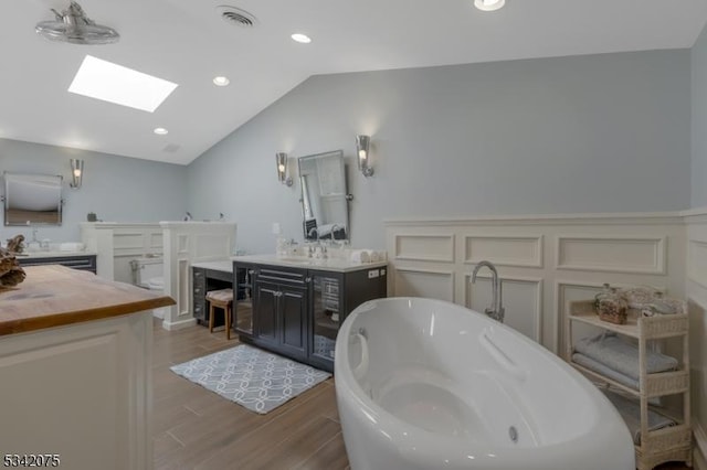 full bath featuring lofted ceiling with skylight, visible vents, a freestanding tub, wood finished floors, and vanity