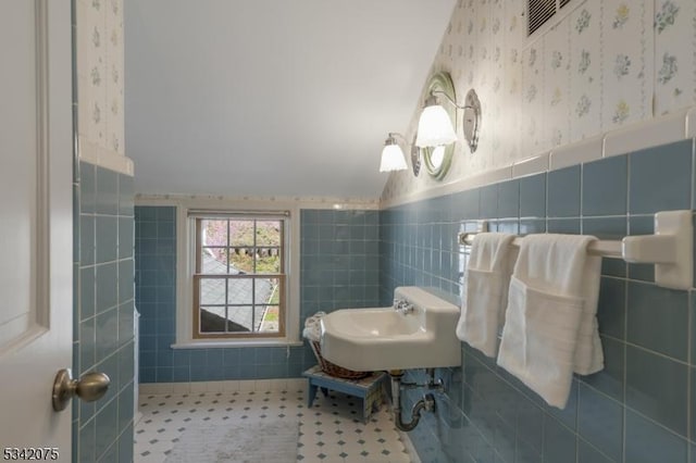 bathroom featuring a wainscoted wall, a sink, tile walls, visible vents, and wallpapered walls