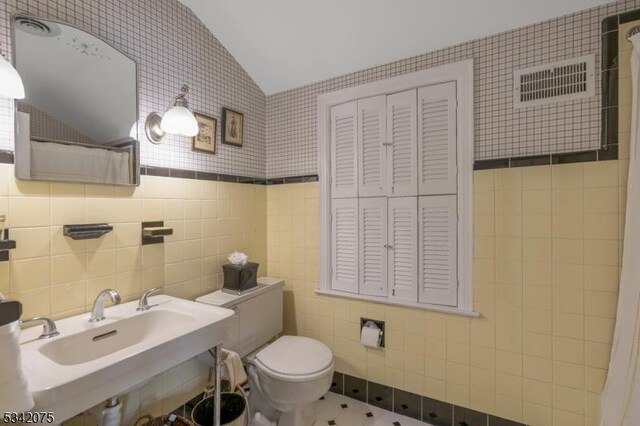 bathroom with a sink, toilet, tile walls, visible vents, and lofted ceiling