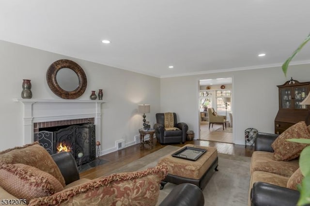 living area featuring wood finished floors, a brick fireplace, crown molding, and visible vents