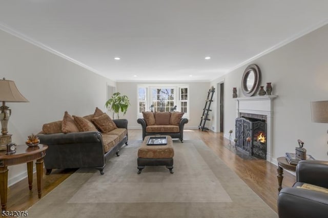living room with recessed lighting, a warm lit fireplace, crown molding, baseboards, and light wood-style flooring