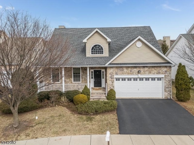 view of front facade featuring driveway, a shingled roof, stone siding, an attached garage, and covered porch