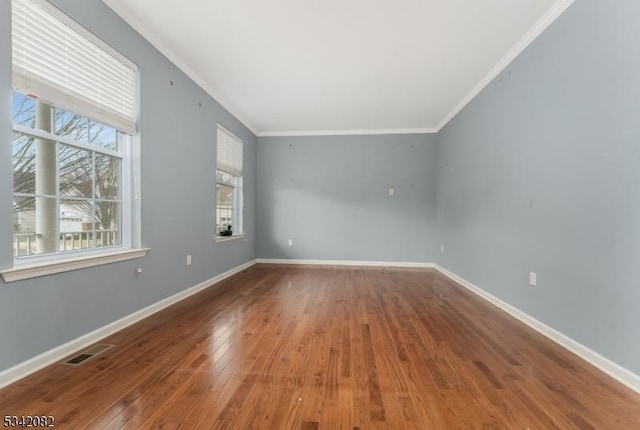 spare room featuring ornamental molding, wood-type flooring, visible vents, and baseboards