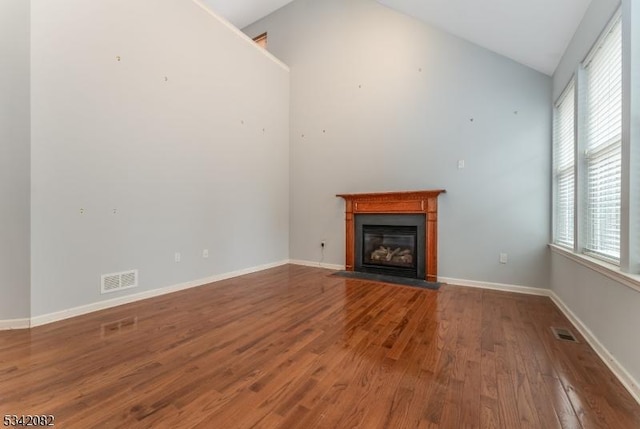 unfurnished living room featuring wood finished floors, a fireplace with flush hearth, visible vents, and baseboards