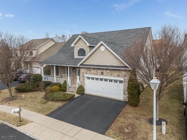 traditional home featuring roof with shingles, a porch, a garage, stone siding, and driveway