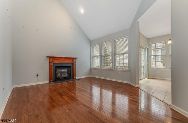 unfurnished living room featuring hardwood / wood-style flooring, a fireplace with flush hearth, high vaulted ceiling, and baseboards