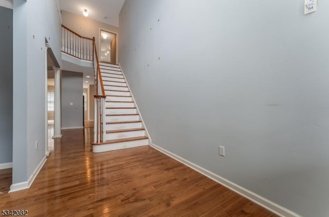 stairs with wood finished floors, a towering ceiling, and baseboards