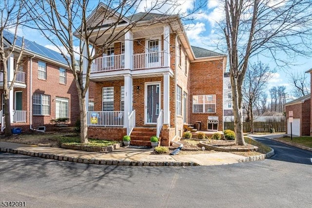 neoclassical / greek revival house with covered porch, brick siding, and a balcony