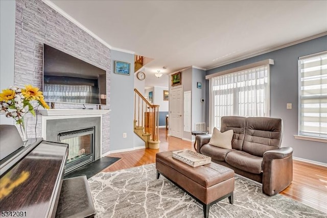 living area with a large fireplace, stairs, ornamental molding, and wood finished floors