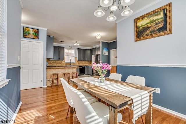 dining space featuring a chandelier, ornamental molding, light wood-type flooring, and baseboards