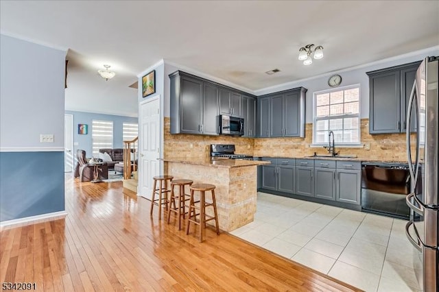 kitchen featuring stainless steel appliances, a sink, a peninsula, and ornamental molding