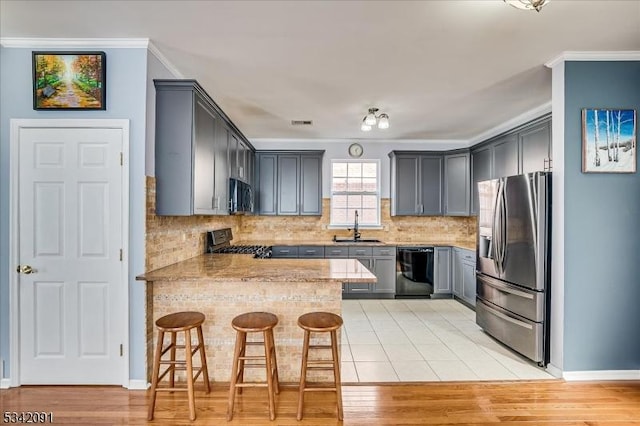 kitchen featuring a peninsula, stainless steel appliances, crown molding, gray cabinetry, and a sink