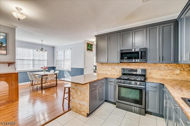 kitchen with a breakfast bar, crown molding, tasteful backsplash, appliances with stainless steel finishes, and a peninsula