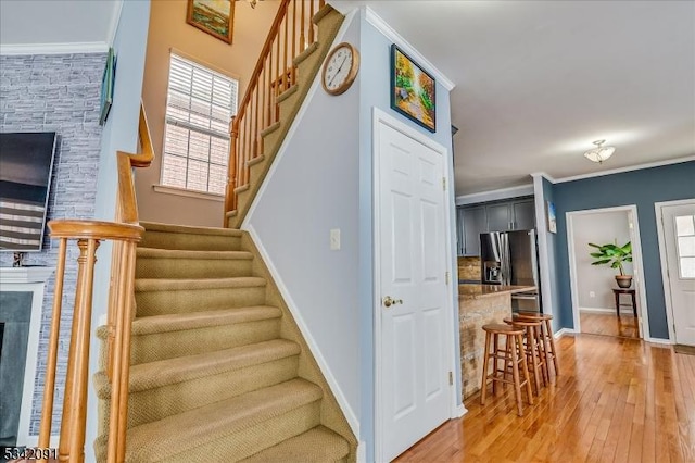 staircase featuring baseboards, a stone fireplace, wood-type flooring, and crown molding