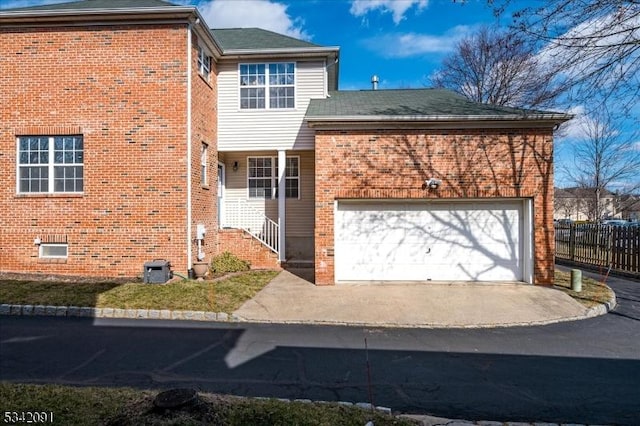 view of front facade featuring brick siding, driveway, an attached garage, and fence