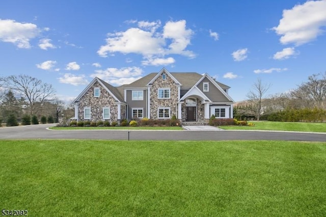 view of front facade with stone siding, a front yard, and driveway