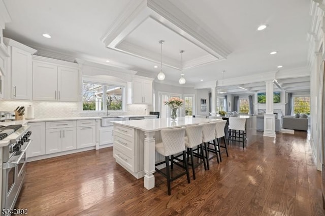 kitchen featuring range with two ovens, a raised ceiling, white cabinetry, and ornate columns