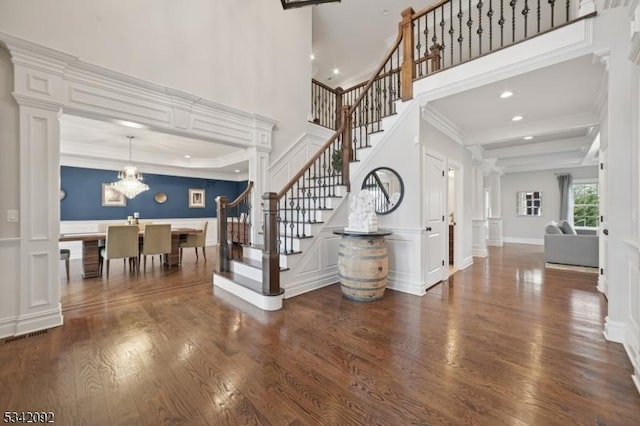 entrance foyer featuring crown molding, decorative columns, a decorative wall, wood finished floors, and stairs