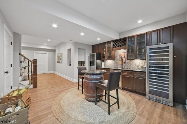 kitchen with light wood finished floors, dark countertops, backsplash, dark brown cabinets, and beverage cooler