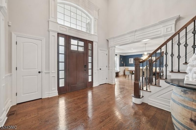 entryway with stairway, wood finished floors, a high ceiling, a chandelier, and a decorative wall