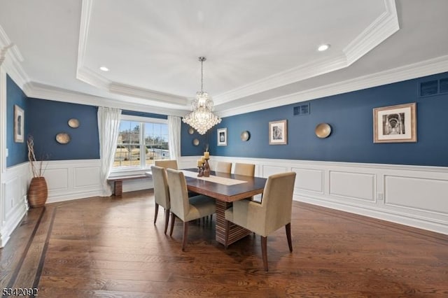 dining area featuring a notable chandelier, a wainscoted wall, visible vents, dark wood finished floors, and a raised ceiling