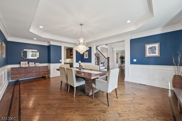 dining area with a notable chandelier, wood finished floors, wainscoting, a tray ceiling, and decorative columns