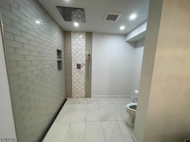 bathroom featuring toilet, baseboards, visible vents, and a tile shower