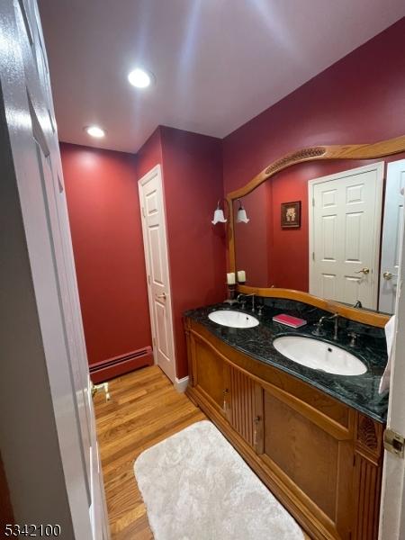 full bathroom with double vanity, wood finished floors, baseboard heating, and a sink