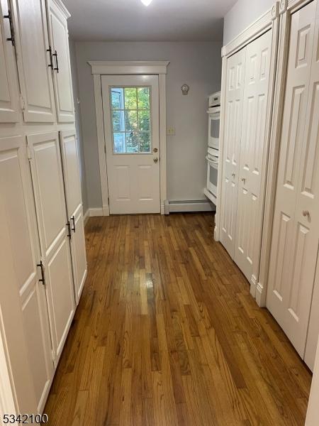 doorway featuring a baseboard heating unit, wood finished floors, and baseboards