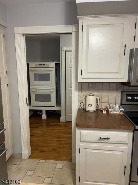 kitchen featuring stainless steel electric range oven, dark countertops, backsplash, multiple ovens, and white cabinets