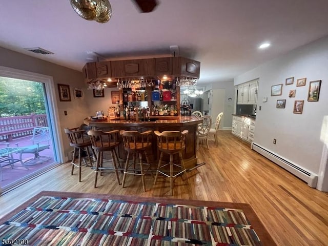 bar featuring light wood-style flooring, visible vents, baseboard heating, and indoor bar