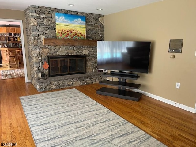 living area with a stone fireplace, baseboards, and wood finished floors