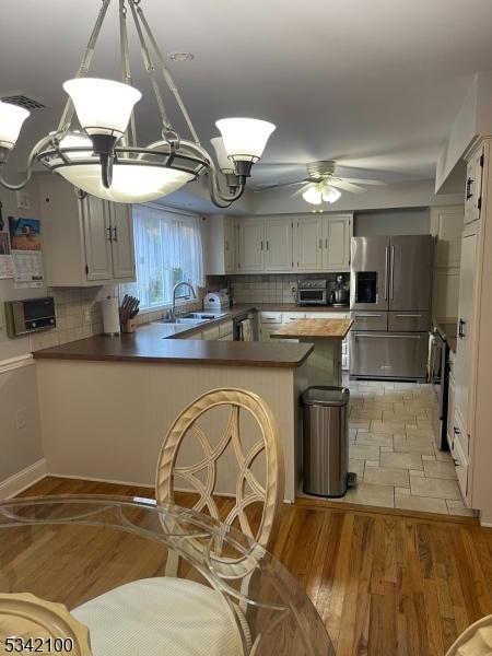 kitchen with a peninsula, decorative backsplash, a sink, and stainless steel fridge with ice dispenser