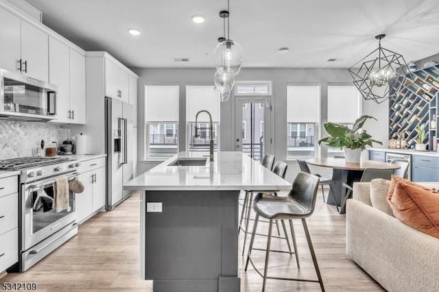 kitchen with a breakfast bar, stainless steel appliances, light countertops, light wood-style flooring, and a sink