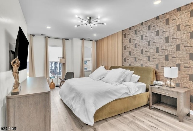 bedroom with light wood-style flooring, an accent wall, a notable chandelier, and recessed lighting