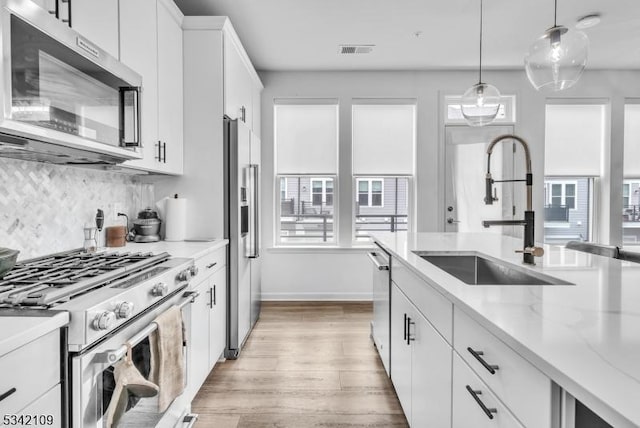 kitchen featuring light wood-style flooring, a sink, visible vents, appliances with stainless steel finishes, and decorative backsplash