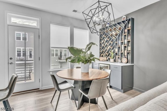 dining space with a dry bar, light wood finished floors, visible vents, a chandelier, and baseboards