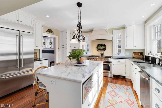 kitchen with white cabinets, custom range hood, a sink, and built in appliances