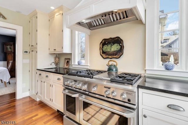 kitchen featuring range with two ovens, a sink, light wood-style floors, custom exhaust hood, and dark countertops