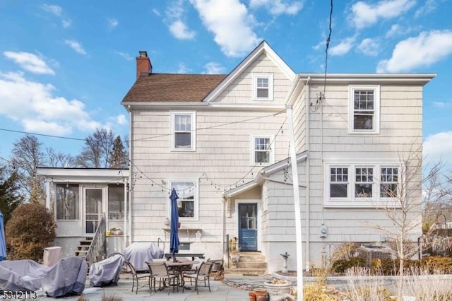 back of house with entry steps, a sunroom, a patio area, and a chimney