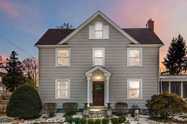 colonial home featuring a shingled roof and a chimney